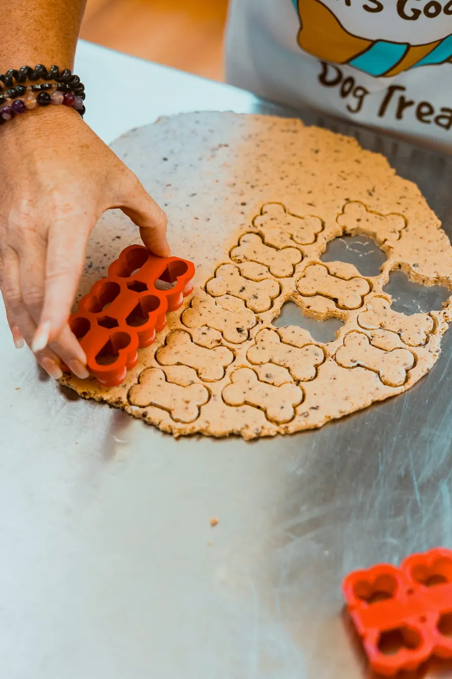 Hands cutting bone-shaped dog treats from dough